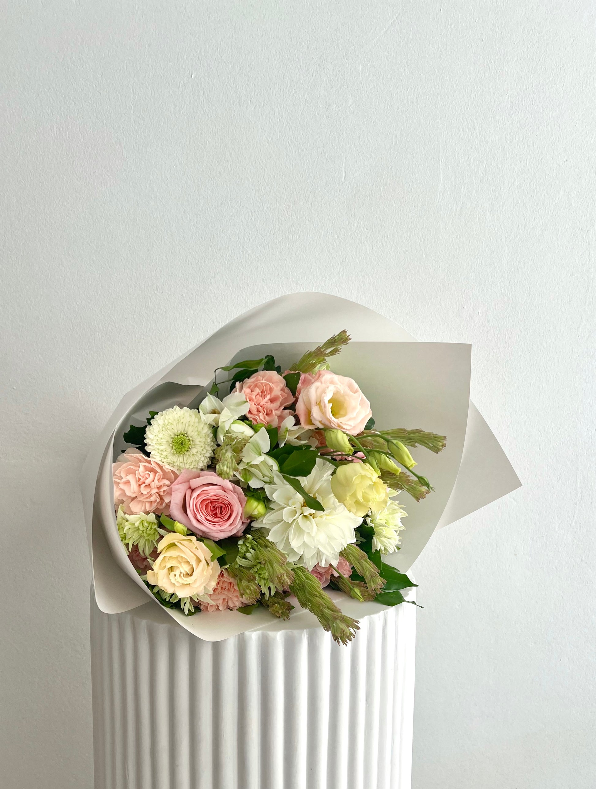 A bouquet of pastel flowers wrapped in white paper on a white plinth