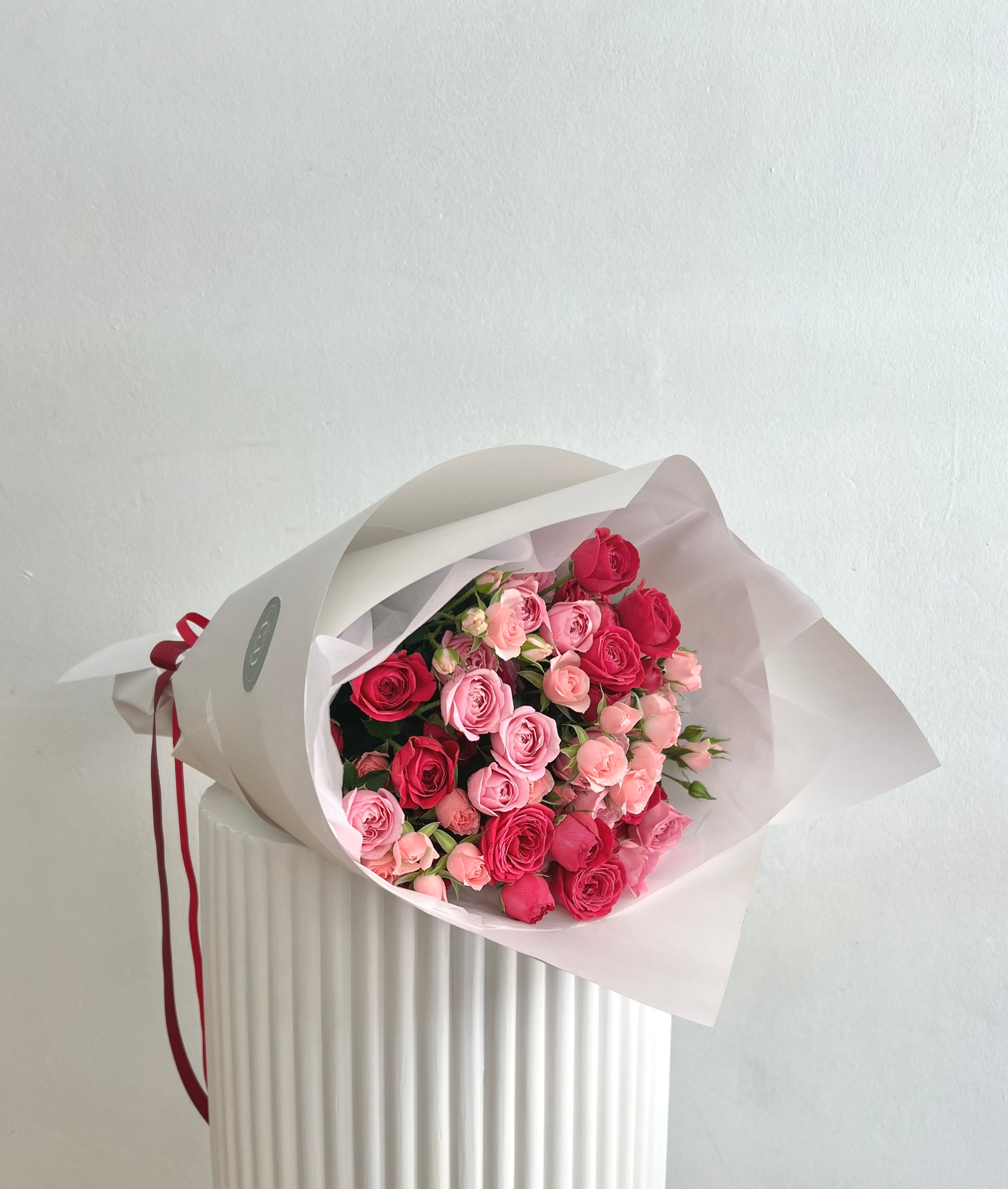 Bouquet of pink and red spray roses wrapped in white paper and a matching ribbon
